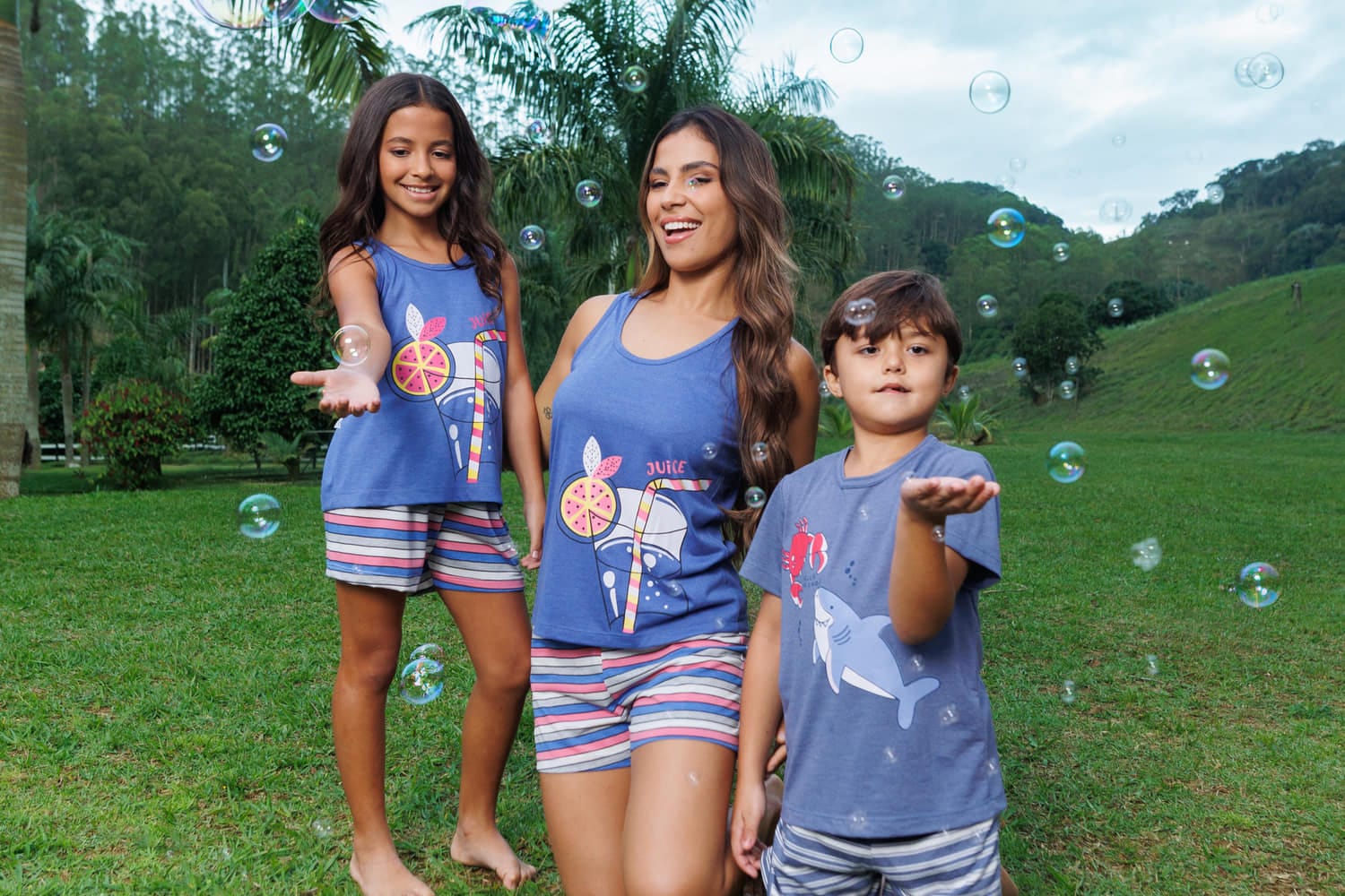 Mãe e dois filhos com pijama curto estampado azul no gramado, coleção Delícias de Verão